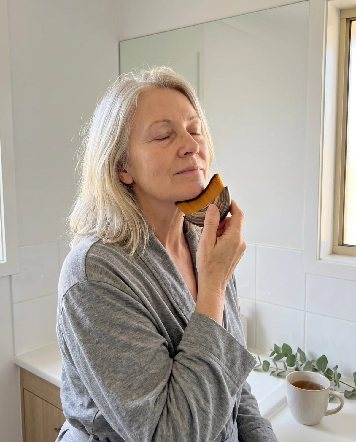 A woman in her sixties using the Wakely brush along her jaw in her bathroom in the morning